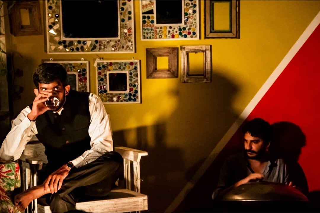 A scene from The Patriarch: an actor in a waistcoat sits beside a wall of mosaic mirrors while Ashim Bery plays a handpan against a red wall
