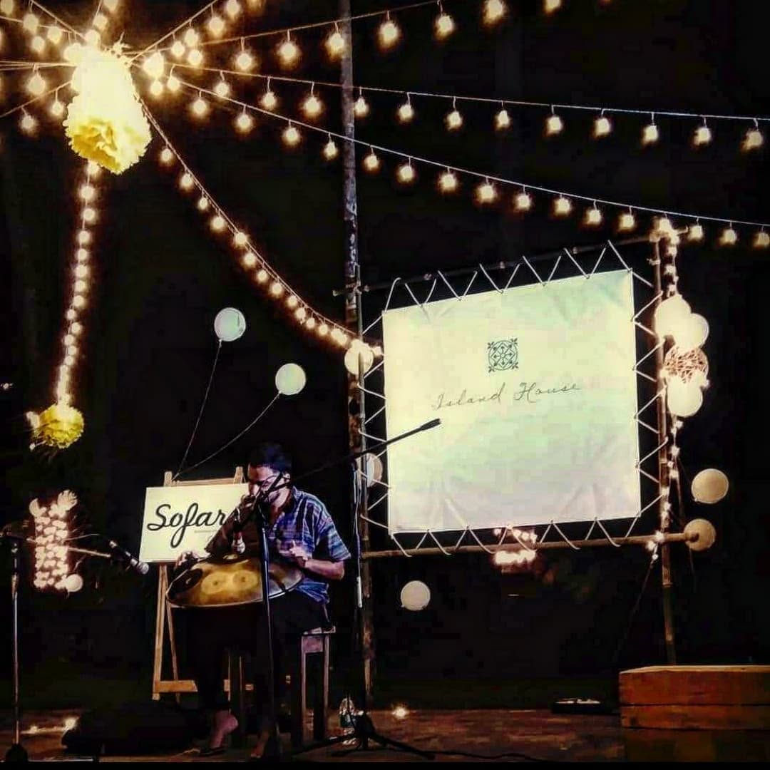 Ashim Bery playing a handpan at night at a Sofar Sounds event, under strings of lights and paper lanterns