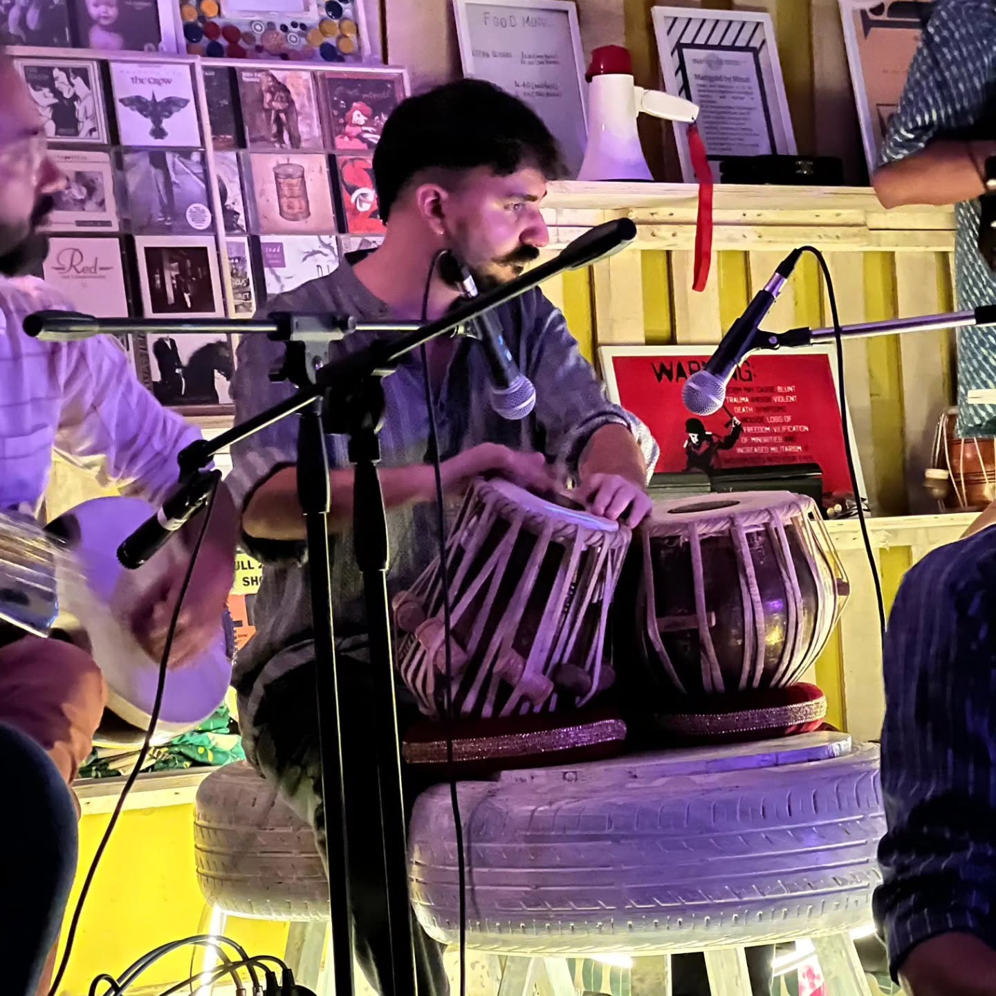 Ashim Bery playing tabla in a crowded music café, between other musicians