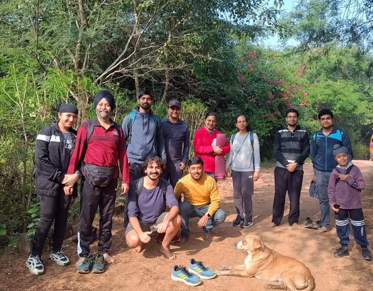 A walking group of all ages smiling on a forest path, from a young child to older adults, with a dog lying in front